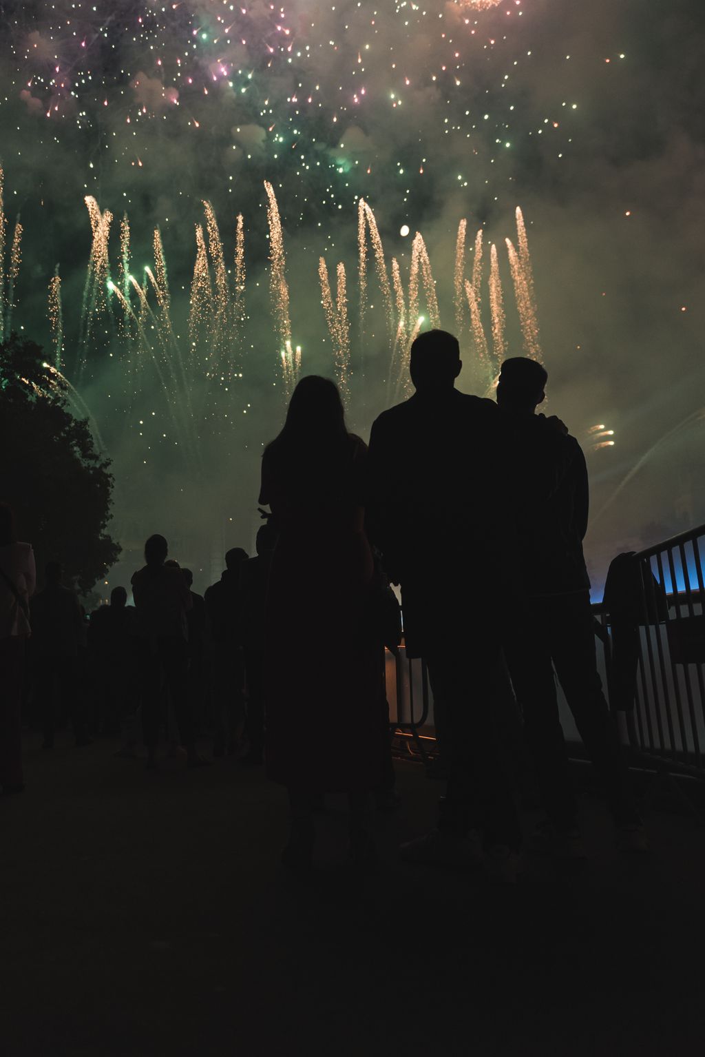 Silueta de tres persones, d’esquena. De fons, els focs artificials del Piromusical de la Mercè 2023.