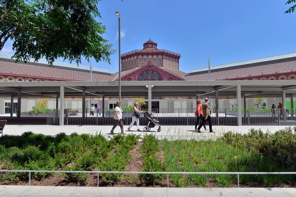 Veïns passejant per la zona pacificada de la superilla de Sant Antoni davant del mercat amb uns grans parterres amb plantes.