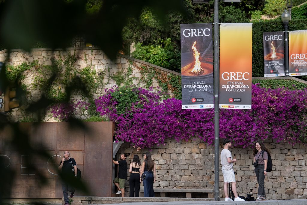 Asistentes a la inauguración del Grec esperan en la entrada del Teatre Grec bajo unas banderolas de la edición del 2024.