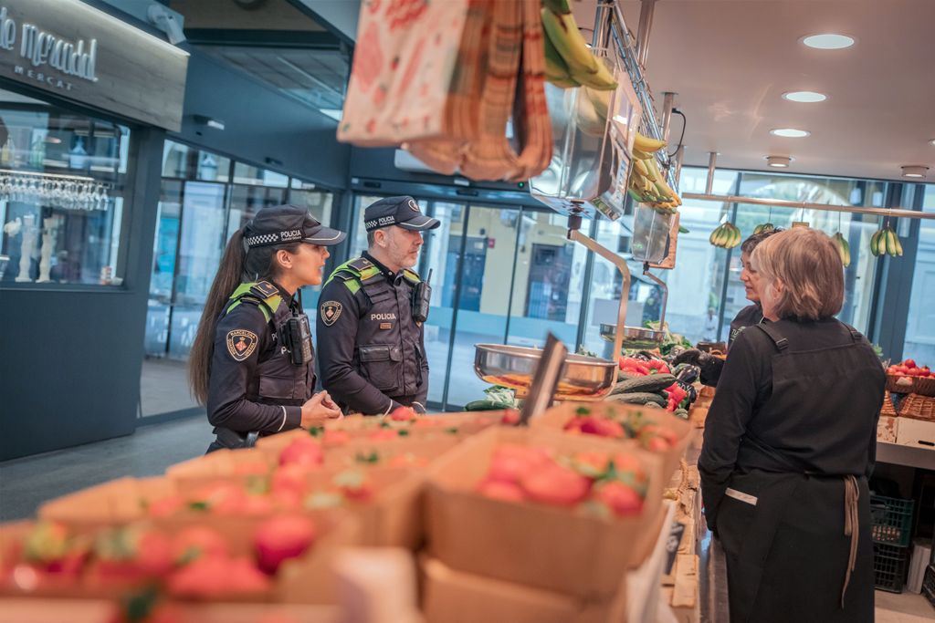 Una pareja de agentes de la Guardia Urbana conversa con las dependientas de un puesto de fruta y verdura del mercado.