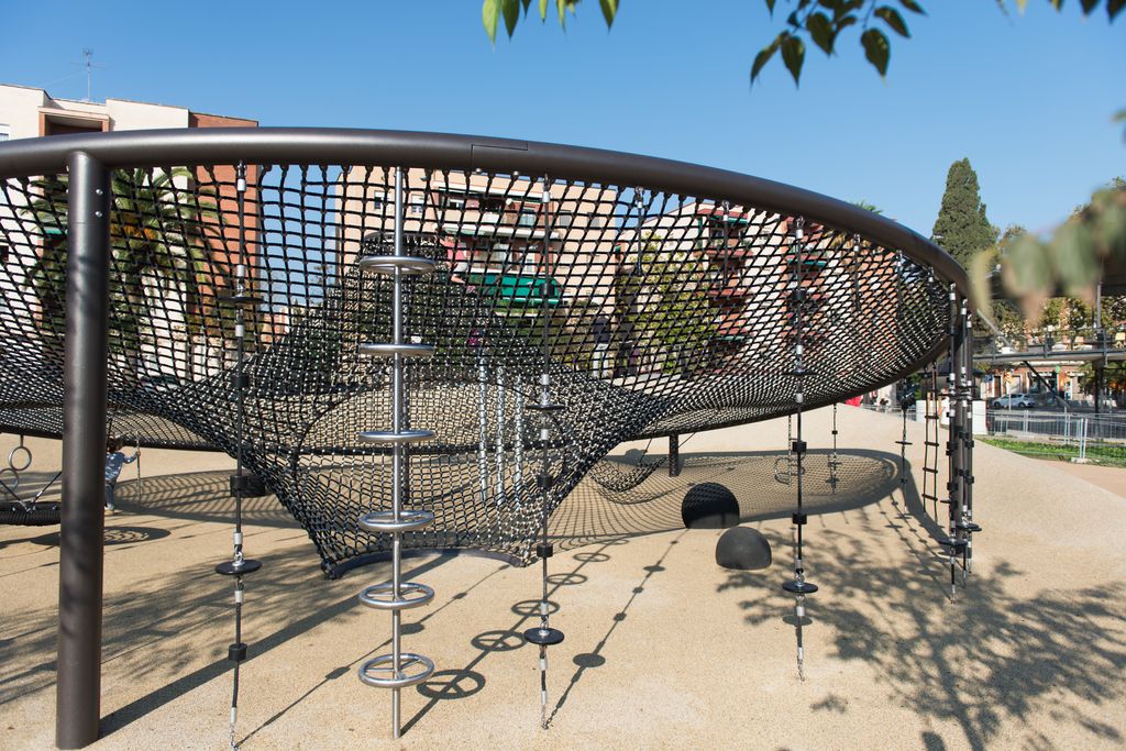 Área de juego infantil de grandes dimensiones que ofrece diferentes posibilidades de juego y de exploración para niños y niñas, formada por una red de actividades lúdicas para jugar por encima y por debajo, de la plaza del Canòdrom