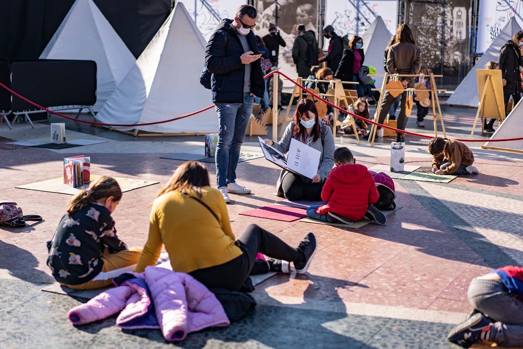 Famílies assegudes a la plaça de Catalunya pintant i llegint en una de les activitats del Festival de Nadal