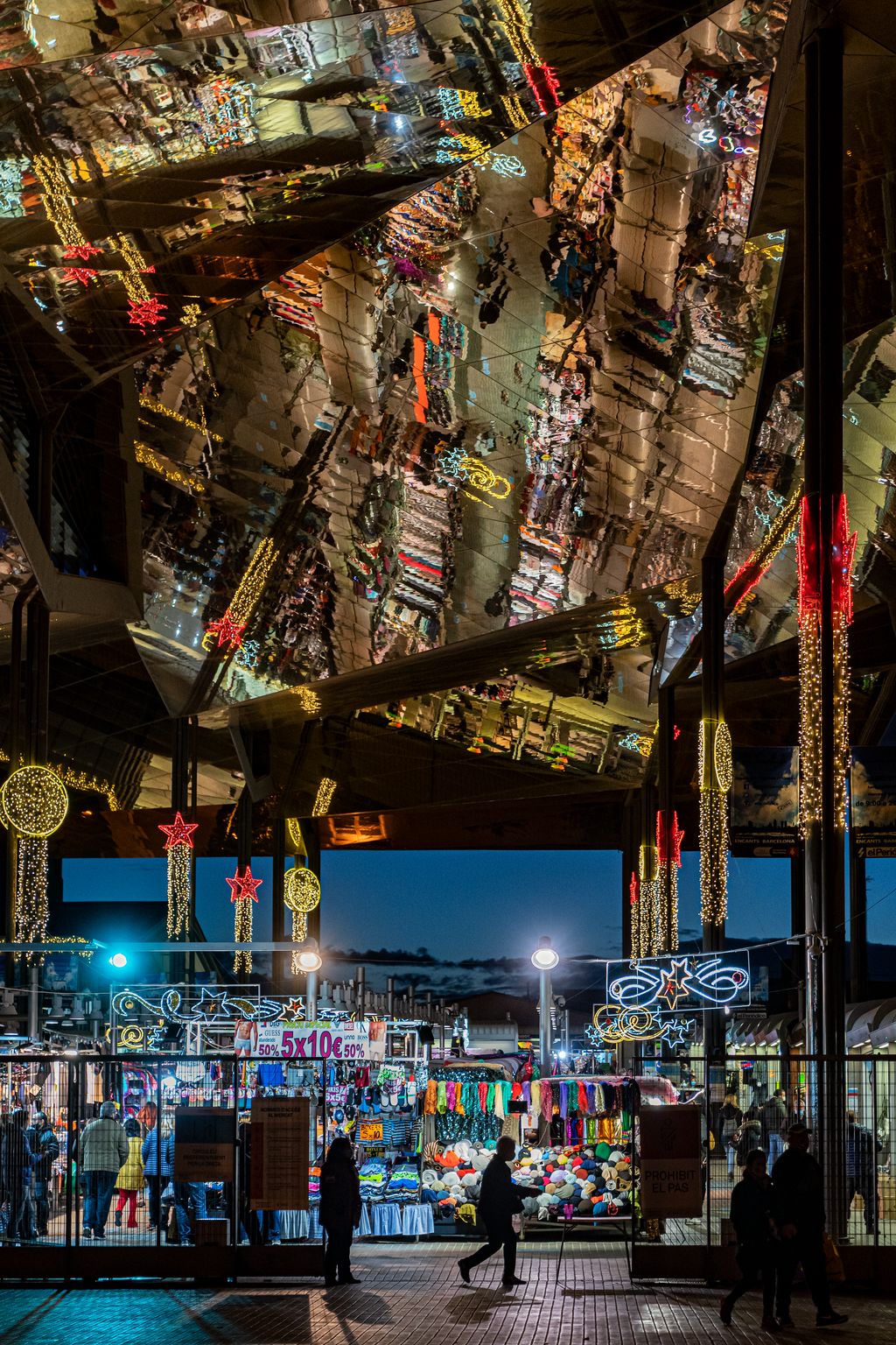 Gent entrant i sortint del Mercat dels Encants il·luminat amb els llums de Nadal