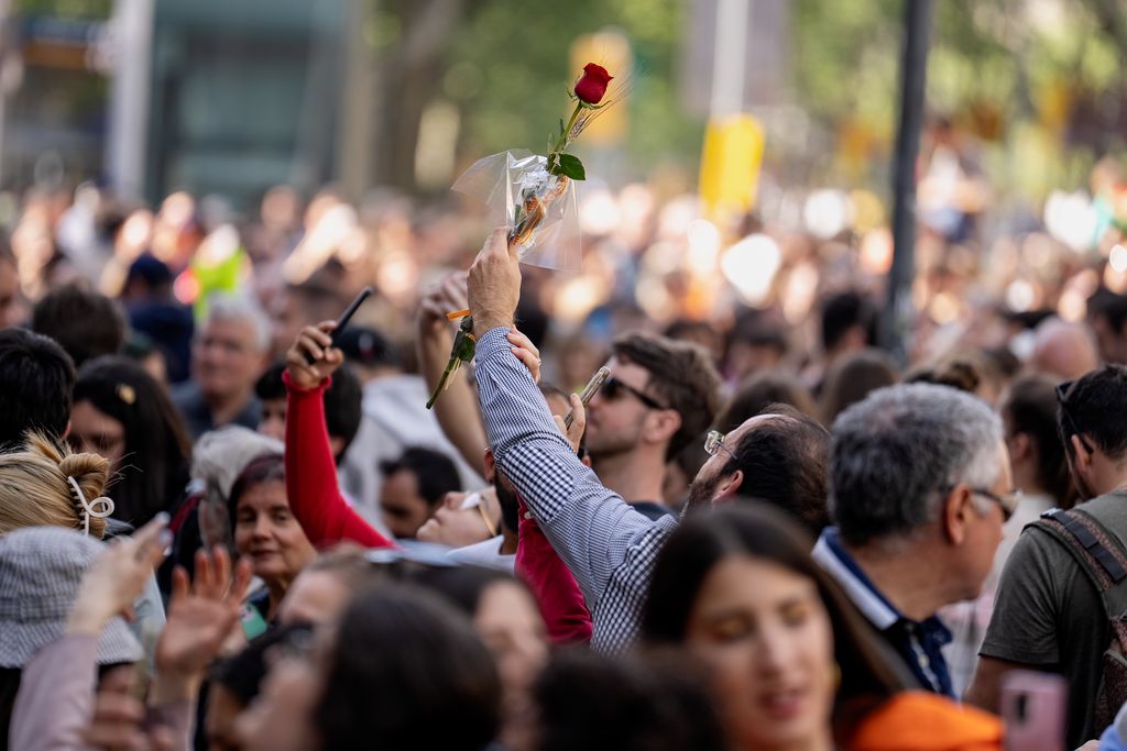 Un home alça una rosa, davant de la casa Batlló, mentre molta gent al seu voltant fa fotografies amb el telèfon mòbil.