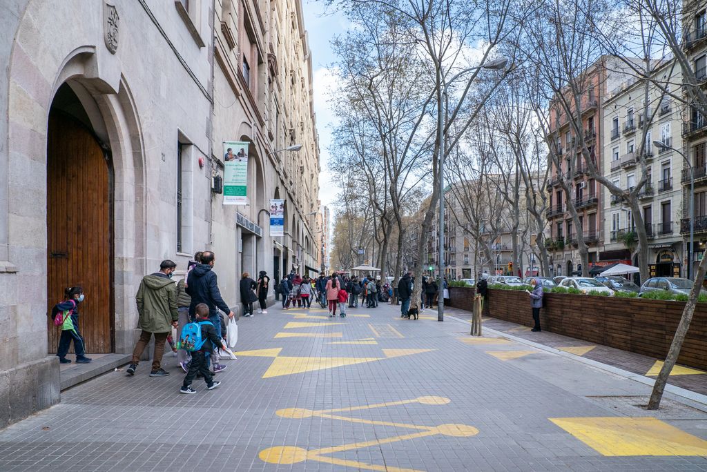 Les famílies passen a buscar els alumnes a la sortida de classe a l’Escola Pia Sant Antoni, a la ronda de Sant Pau. Davant de l’entrada s’ha ampliat la vorera ocupant un carril per construir-hi una plataforma de fusta que separa la zona del trànsit de vehicles, i a la vorera hi ha unes figures grogues