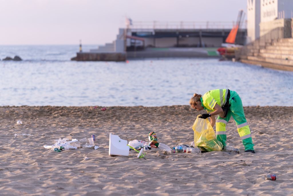 Una trabajadora del servicio de limpieza recogiendo, en una bolsa de plástico, los envases que han dejado sobre la arena durante la verbena