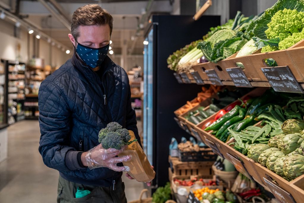 Un home posa un bròquil que vol comprar a granel dins d’una bossa de paper