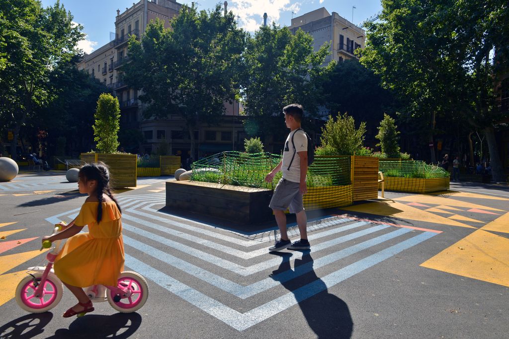 Una nena va en bicicleta per una zona de jocs de la superilla de Sant Antoni delimitada per jardineres i amb el paviment pintat en diferents colors