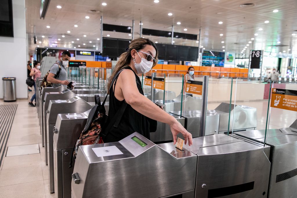 Gent amb mascareta validant els títols de viatge per entrar a la zona del vestíbul de Rodalies de l'estació de Sants