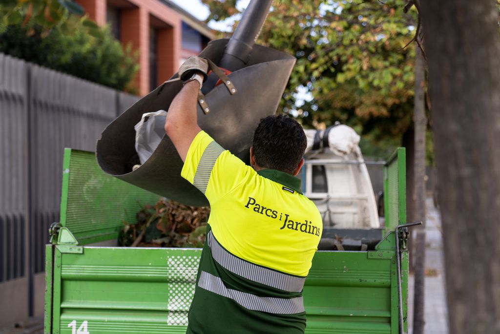 Un treballador de neteja de Parcs i Jardins carrega a la camioneta el cistell recollidor i el bufador de fulles.