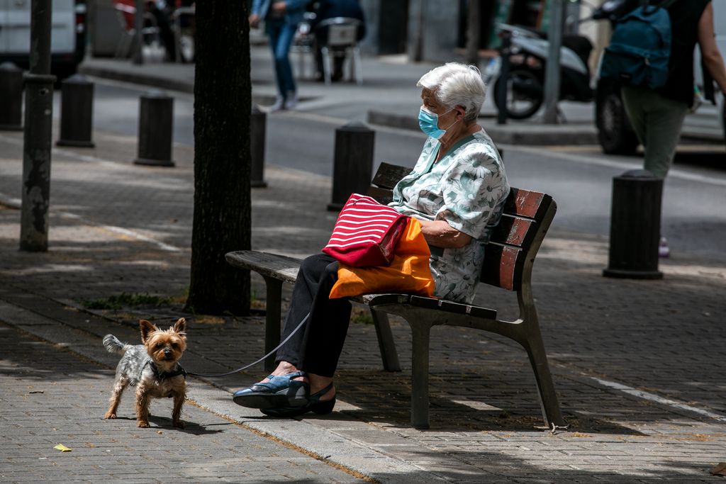 Una dona descansa en un banc a la via Júlia durant el passeig amb el seu gos