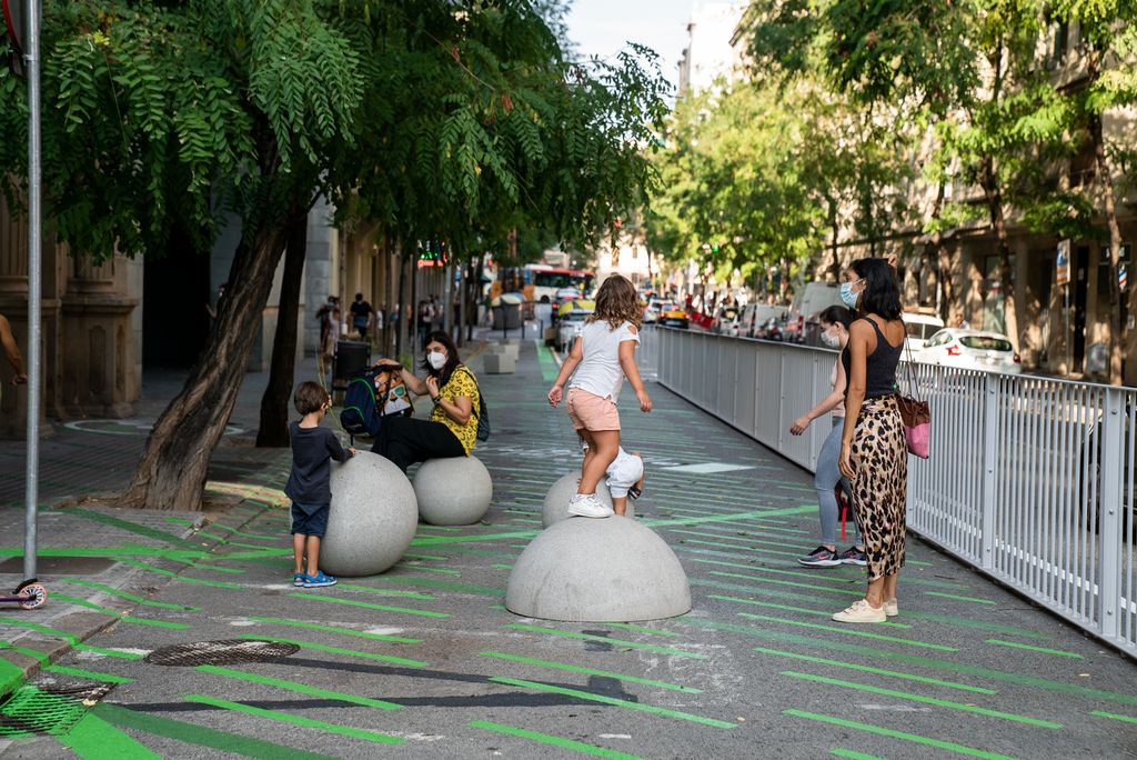 Nens jugant a les semiesferes i esferes col·locades a la zona pacificada davant de l’Escola Pia Balmes sota la mirada de les seves famílies