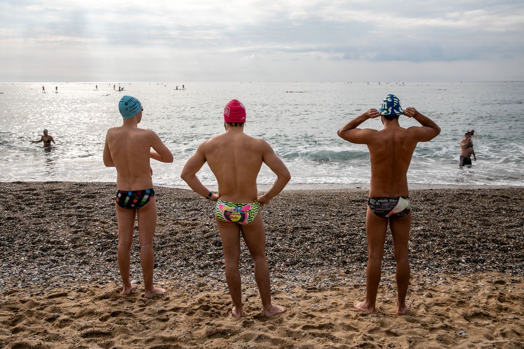 Tres nedadors amb casquet es preparen a la platja abans d'entrar a l'aigua