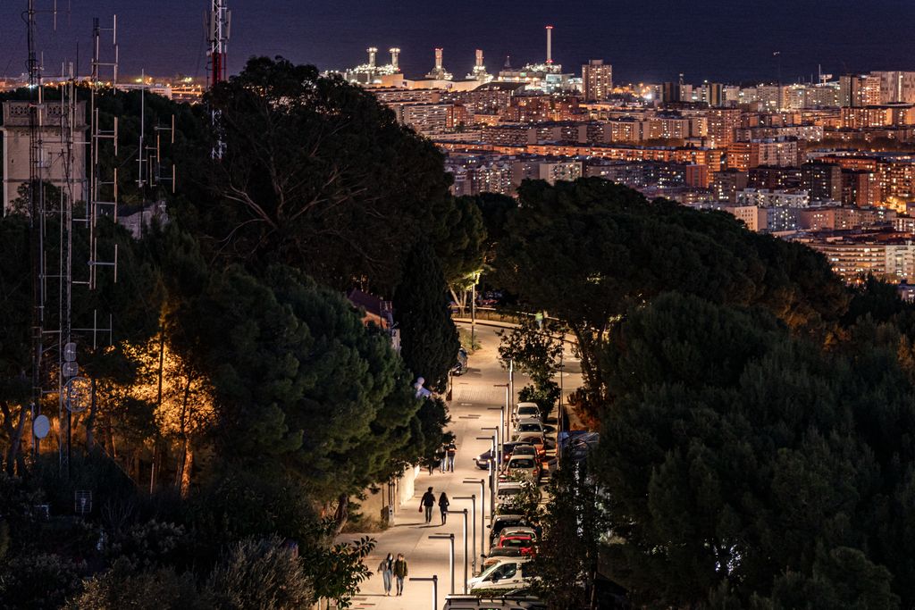 Fotos nocturnas de la ciudad. Panorámica de Barcelona desde los búnquers del Carmel hacia el mar. Se ven personas caminando por una calle bien iluminada y coches aparcados a un lado