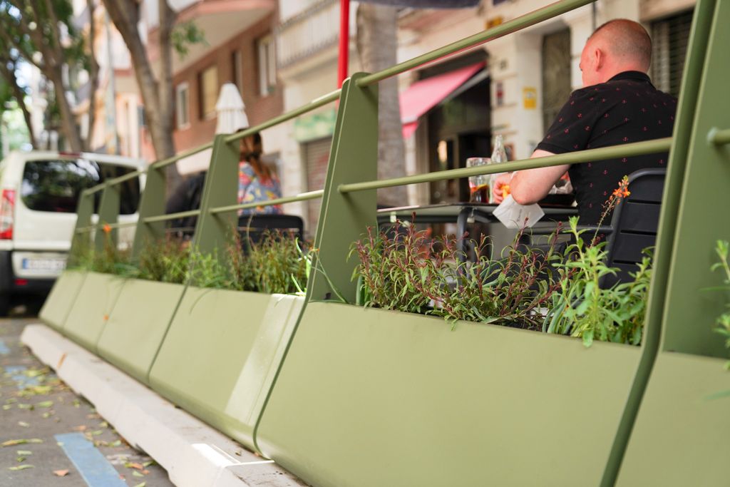 Client assegut consumint una beguda en un dels nous prototips de terrasses en línia de Barcelona, amb unes barreres metàl·liques amb jardineres que la separen de la calçada i el trànsit de vehicles