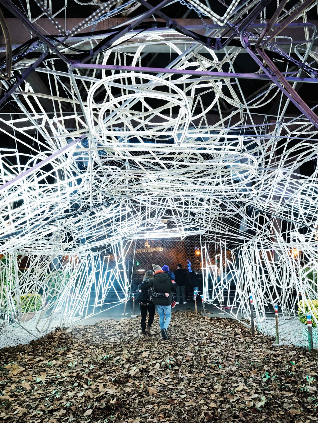 Famílies sortint del Parc de la Màgia de Nadal amb tubs de llums i amb el terra ple de fulles d'arbres