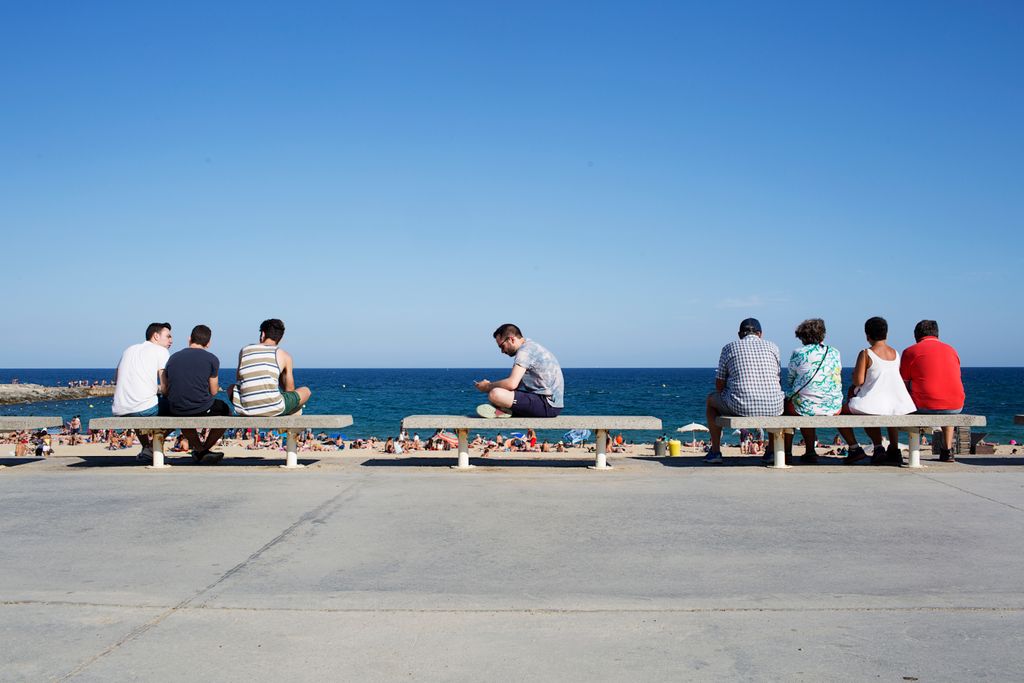 Persones assegudes als bancs del Passeig marítim davant la platja