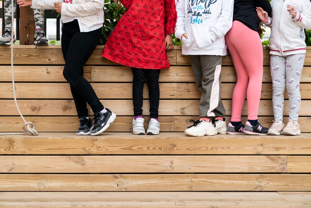 Detall de les cames d'uns infants que juguen a les grades de fusta del pati de l'escola