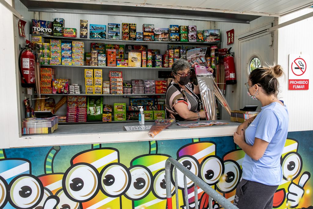 Una dona compra focs artificials i petards per a la revetlla de Sant Joan a un quiosc a la via Júlia. La dependenta li'n mostra alguns. Al seu costat, es veu el gel hidroalcohòlic