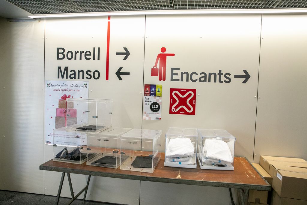 Taula amb urnes, equips de protecció individual i caixes amb paperetes preparades a prop d'un accés del Mercat de Sant Antoni
