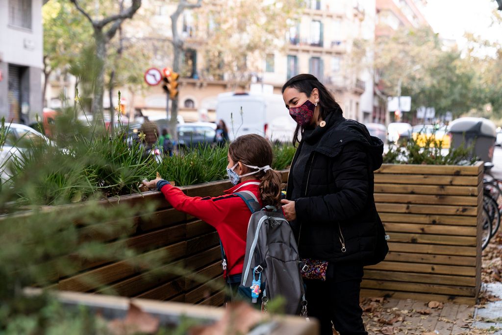 Una nena amb la seva mare al costat mira les plantes de les jardineres instal·lades per separar del trànsit la zona de vorera ampliada davant de la porta de l’Escola Carlit