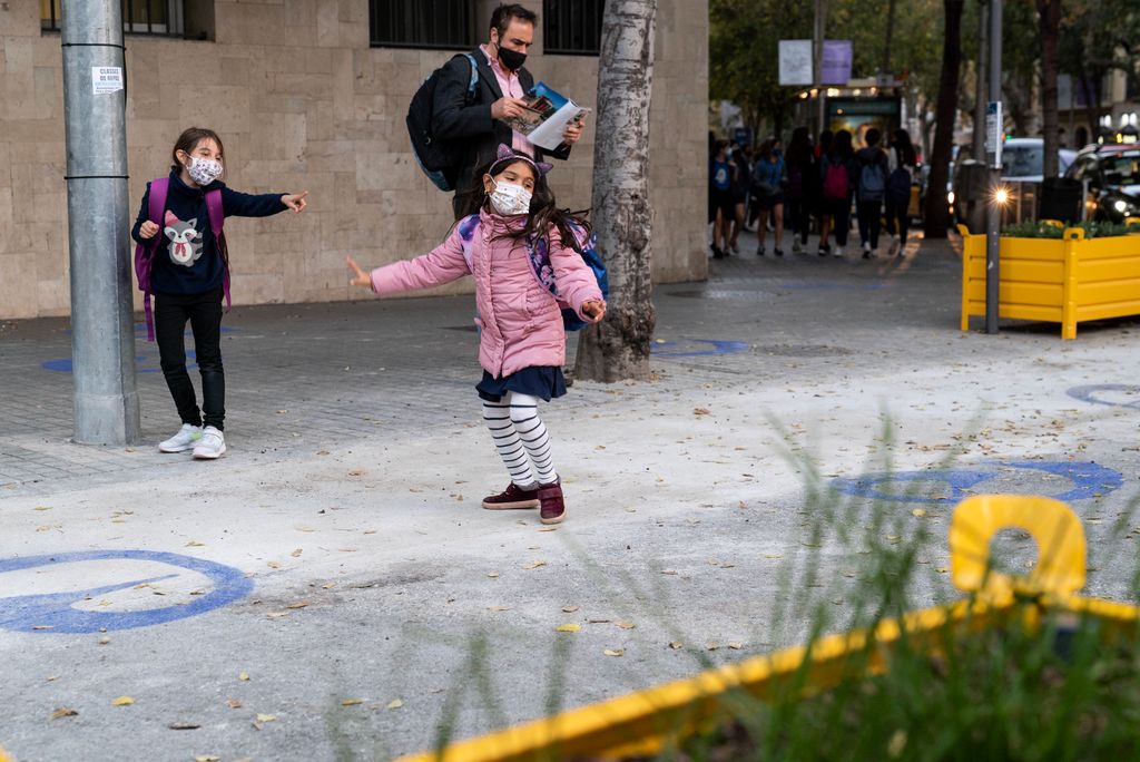 Dues nenes juguen i riuen contentes a la zona pacificada de vorera ampliada de davant del Col·legi Escolàpies de Llúria. Es veuen les jardineres que hi ha al voltant del perímetre i els dibuixos de color lila pintats al paviment