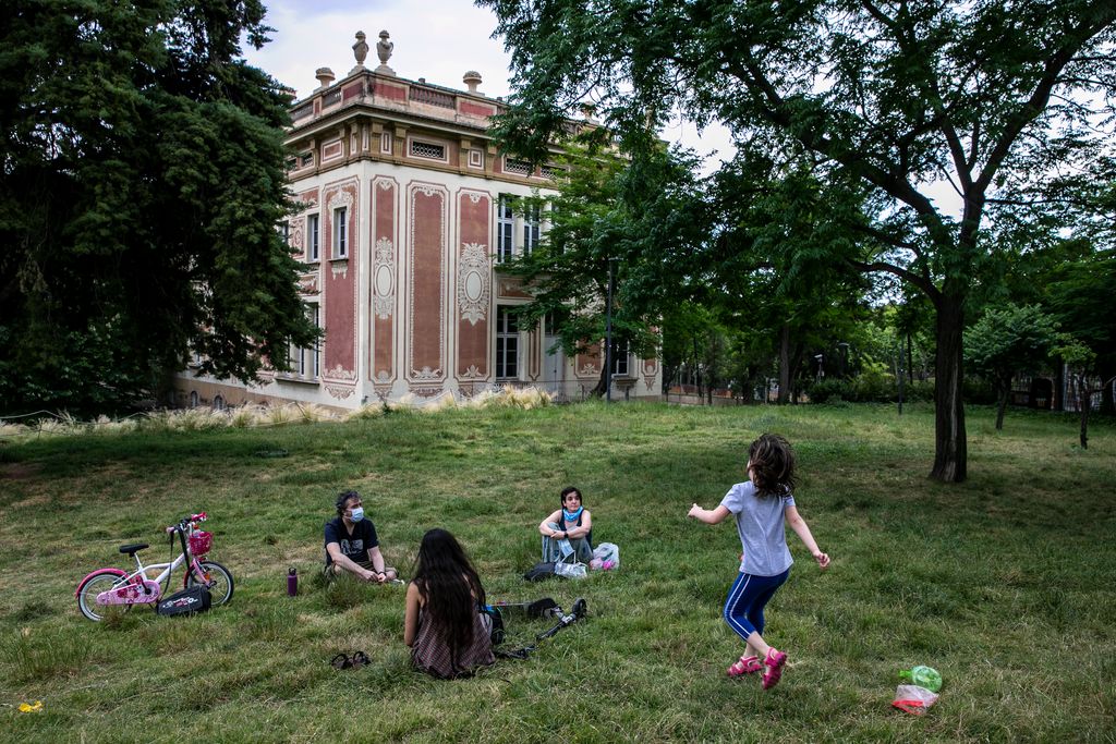 Unes famílies seuen sobre la gespa als jardins de la Maternitat mantenint les distàncies de seguretat mentre els més petits juguen