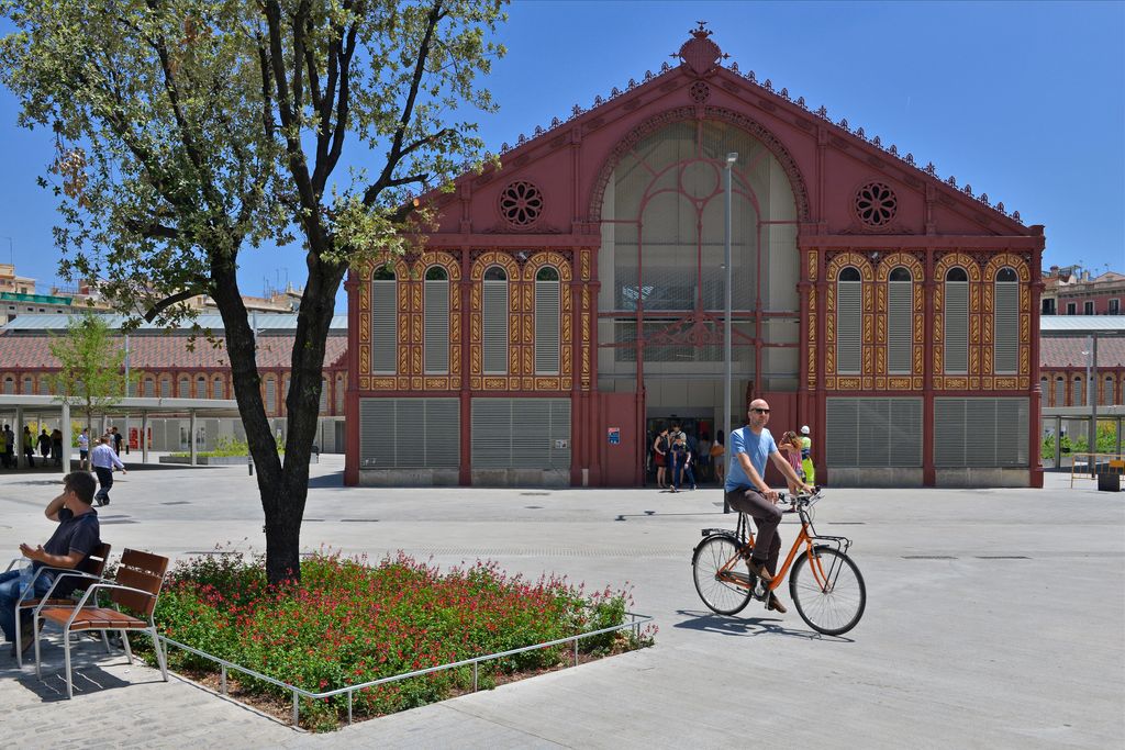 Veïns anant i venint, asseguts als bancs o circulant amb bicicleta per la zona pacificada de la superilla de Sant Antoni davant del mercat