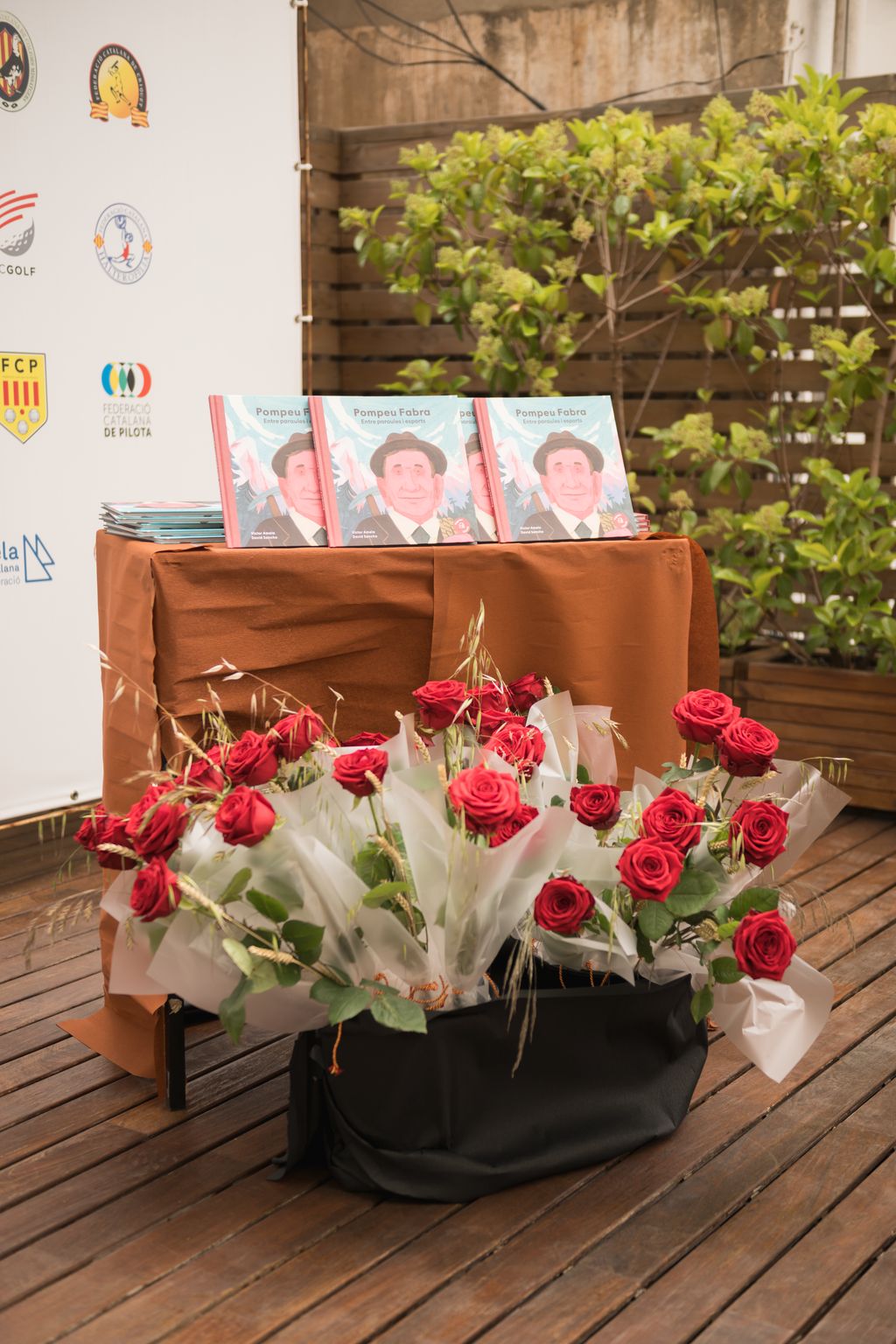 Libros de ‘Pompeu Fabra. Entre palabras y deportes’, de Victor Amela y David Sancho, expuestos y muchas rosas debajo