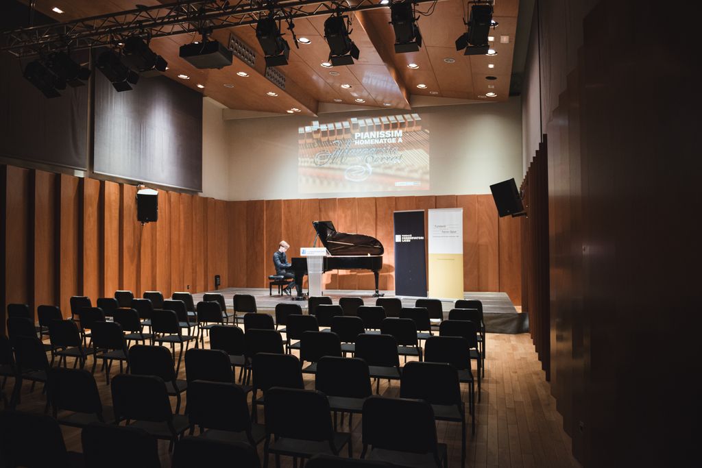Un estudiant toca el piano a l'escenari de la Fundació Conservatori del Liceu. A la pantalla llegim “Pianíssim: homenatge a Margarita Serrat”. Els seients de l'auditori són buits