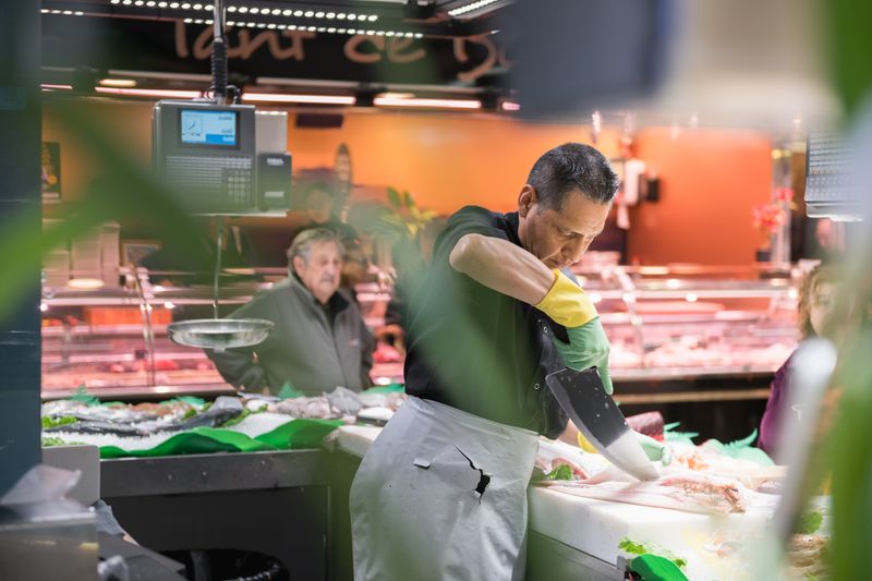 
             Un peixater talla el peix en una peixateria del Mercat de la Marina
             Autor: Ceci Fimia
             Mostra els detalls de la imatge Un peixater talla el peix en una peixateria del Mercat de la Marina
             