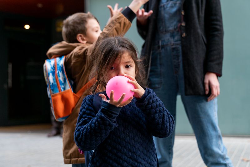 
             Una nena infla un globus a la sortida de l’Escola Carlit
             Autor: Mariona Gil
             Mostra els detalls de la imatge Una nena infla un globus a la sortida de l’Escola Carlit
             